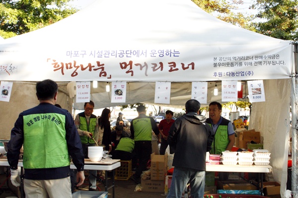 사진설명 : 먹거리코너 운영하는 공단 직원들 모습, 배경 글자 : 마포구시설관리공단에서 운영하는 희망나눔 먹거리코너, 본 공단의 먹거리코너 판매수익금은 불우이웃돕기를 위해 전액 기부됩니다, 후원 다농산업